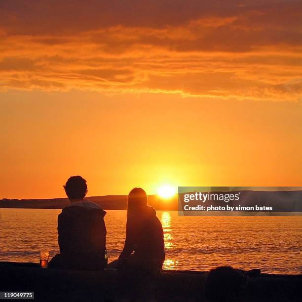 couple watching sunset at  beach - couple sunset beach stock pictures, royalty-free photos & images