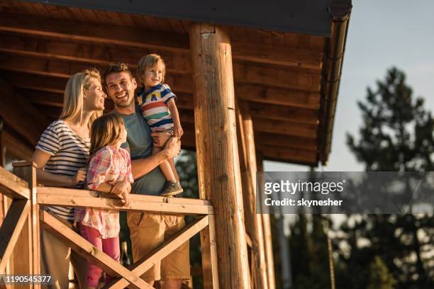 los padres felices y sus hijos pequeños disfrutan en un balcón de su chalet. - chalé fotografías e imágenes de stock