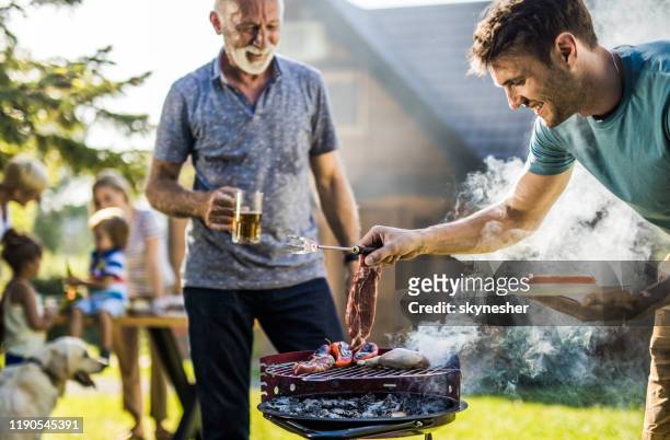 gelukkige man grillen vlees op een barbecue grill buiten. - backyard grilling stockfoto's en -beelden