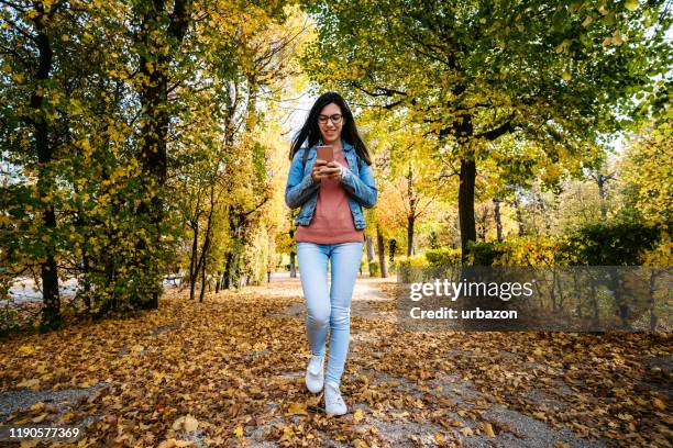 woman texting and walking in a park - woman walks down street stock pictures, royalty-free photos & images