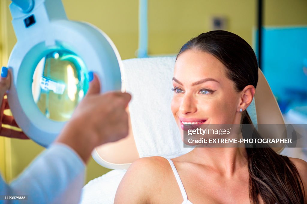 Een mooie jonge vrouw glimlachend op het examen Vergrootglas licht in een cosmetische salon