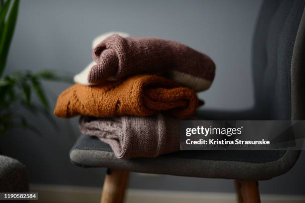 three knitted sweaters on a chair by a green plant - trui stockfoto's en -beelden