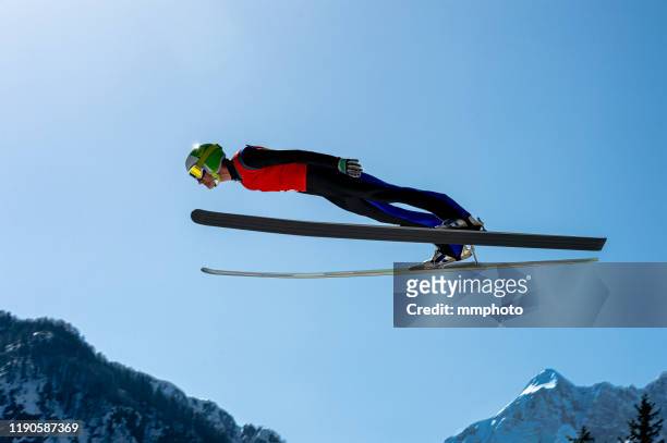 side view of male ski jumper in mid-air - wintersport stock-fotos und bilder