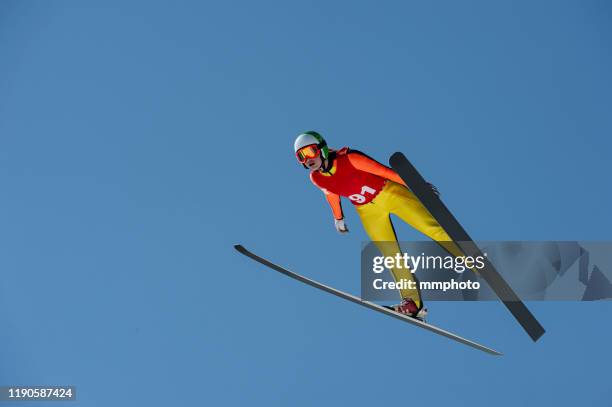 young women in ski jumping action against the blue sky - salto con gli sci foto e immagini stock