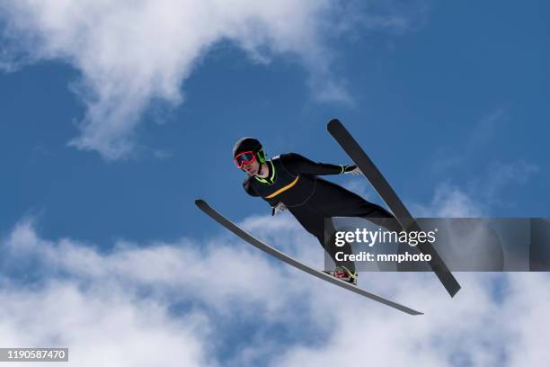 front view of male ski jumper in mid-air against the cloudy sky - skispringen stock-fotos und bilder