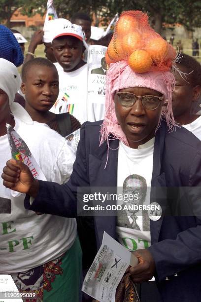 Woman wearing a tee-shirt with a picture of Zimbabwean President Robert Mugabe sings and dance while balancing oranges on her head during a Zanu PF...