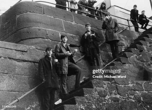 The Beatles, Paul McCartney, Ringo Starr, John Lennon and George Harrison, posing on steps at Liverpool docks with cups of tea, Liverpool, Britain