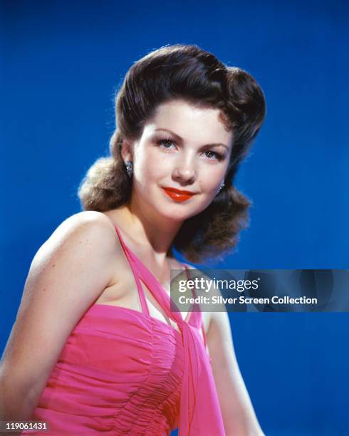 Anne Baxter , US actress, wearing a pink halterneck top in a studio portrait, against a blue background, circa 1945.