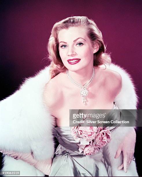 Anita Ekberg, Swedish model and actress, glamorous in a low-cut dress, with flowers covering her cleavage, a white fur stole and a pearl necklace...