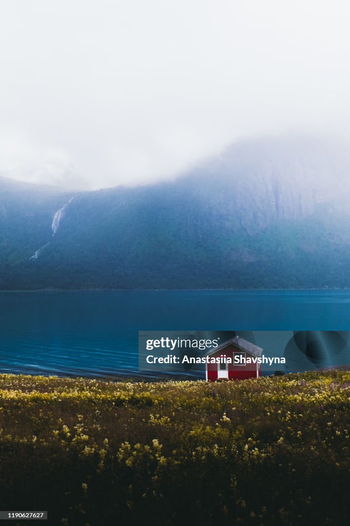 Eenzame verlaten rode huis op de weide met uitzicht op de bergen en de waterval in Noorwegen