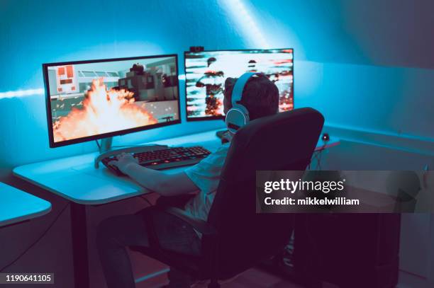 少年はオンラインでビデオゲームをプレイし、2つの大きなコンピュータモニタの前に座ります - media night ストックフォトと画像