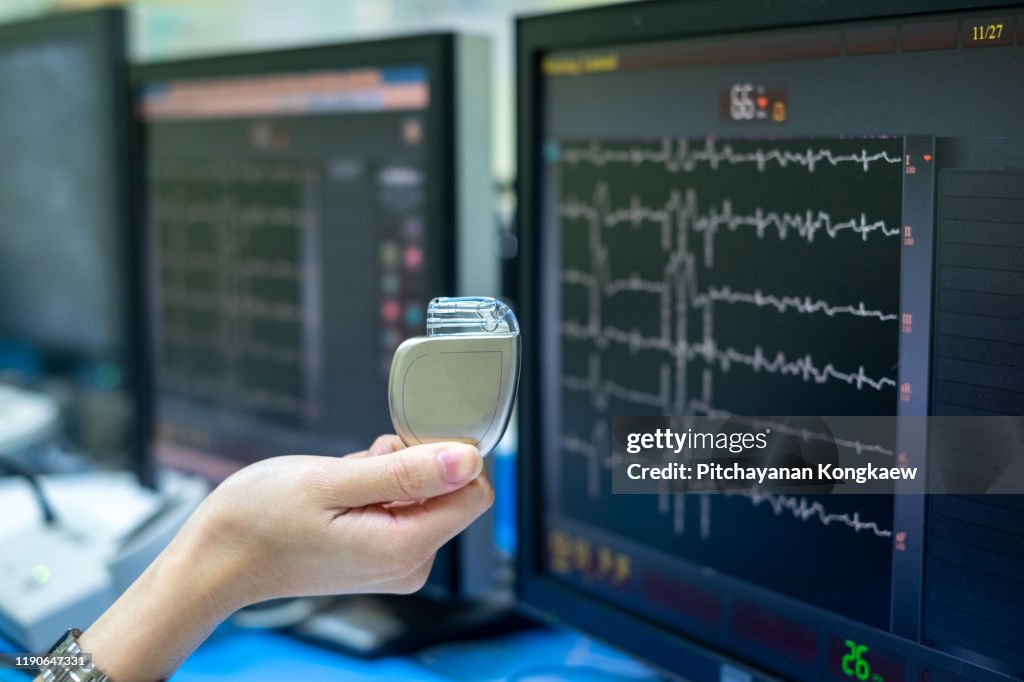 Doctor Hand hold Pacemaker device with screen of EKG monitoring background