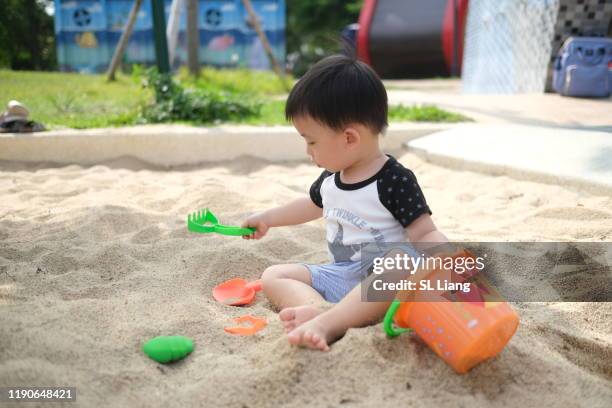 toddler boy shoveling sand into bucket, asian, taiwan - sandkasten stock-fotos und bilder