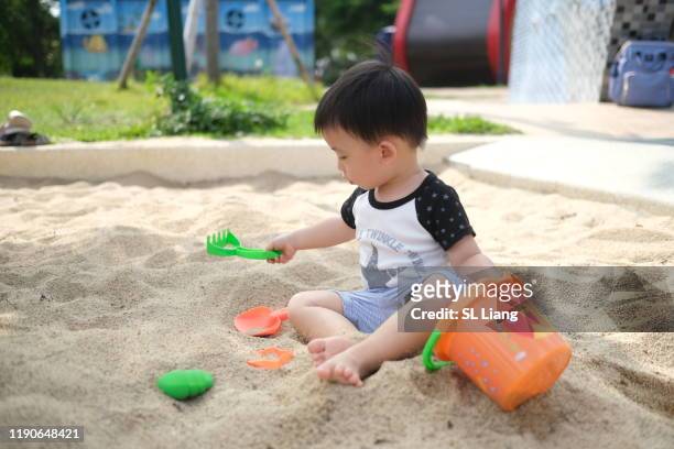 toddler boy shoveling sand into bucket,  asian, taiwan - digging beach photos et images de collection