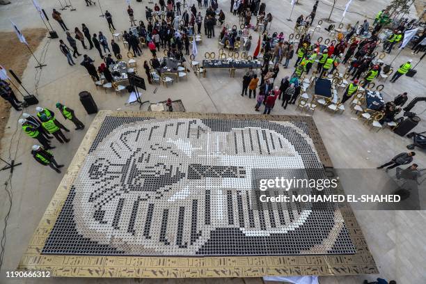 People gather around a depiction of the ancient Egyptian Pharaoh Tutankhamun's death mask made of 7260 cups of coffee, in front of the newly-built...
