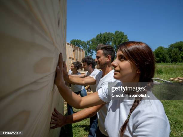 young volunteers lifting up a plywood wall at a construction site for a housing project - habitat for humanity stock pictures, royalty-free photos & images