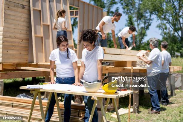 beautiful team of female volunteers looking at a blueprint of a housing project while talking very cheerfully - habitat for humanity stock pictures, royalty-free photos & images