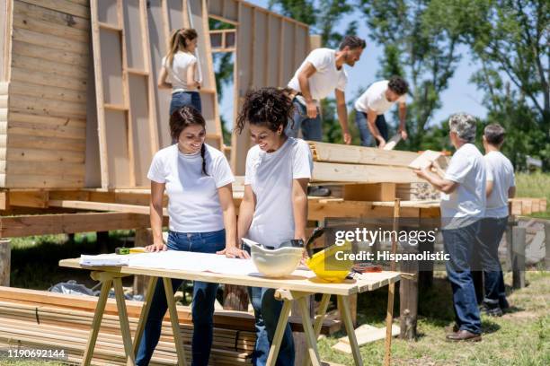 beautiful team of female volunteers looking at a blueprint of a housing project while talking very cheerfully - volunteer building stock pictures, royalty-free photos & images