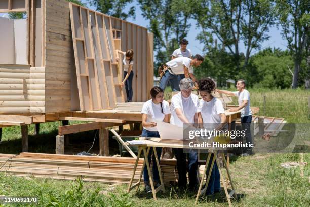 mature male foreman explaining something to volunteers while showing them a blueprint - habitat for humanity stock pictures, royalty-free photos & images