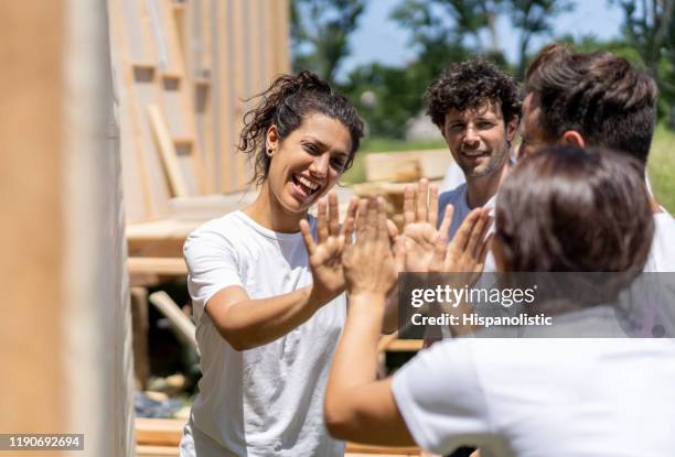 grupo de alegres voluntarios construyendo una casa de caridad celebrando con un alto cinco - hábitat para la humanidad fotografías e imágenes de stock