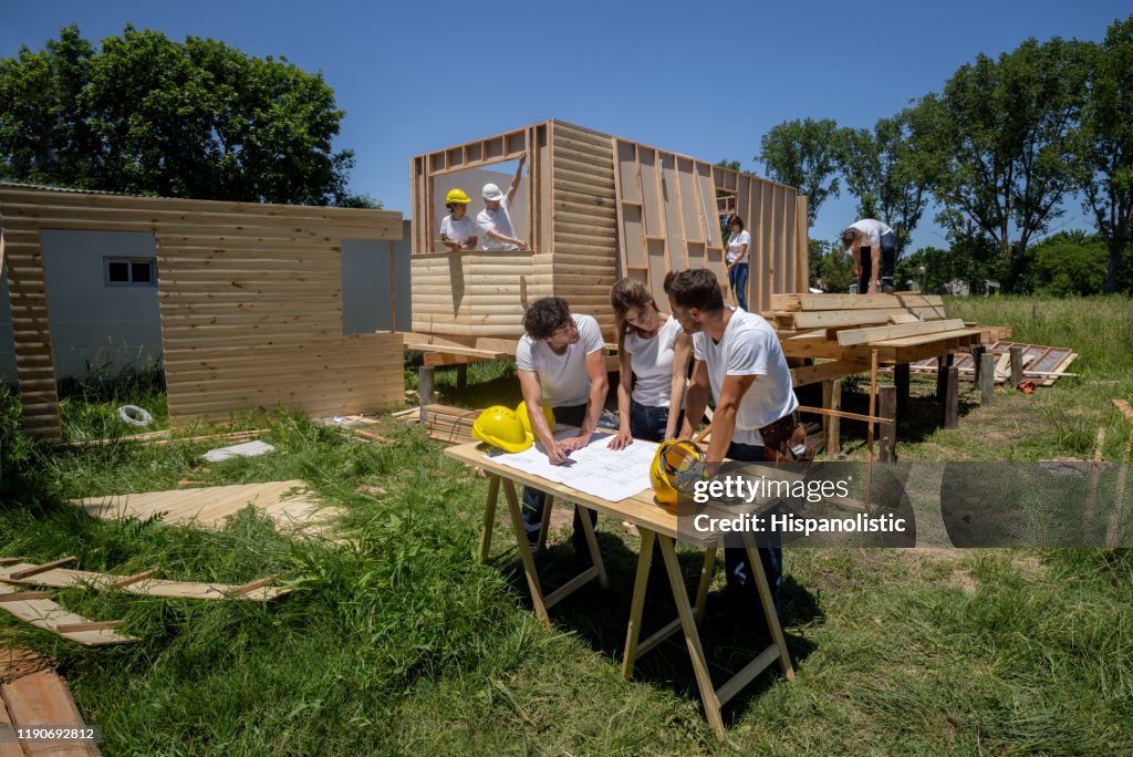 Group of volunteers at a housing project looking at a blueprint while discussing something
