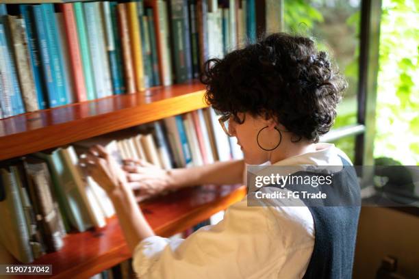 woman searching for a book in a bookshelf - reading nook stock pictures, royalty-free photos & images