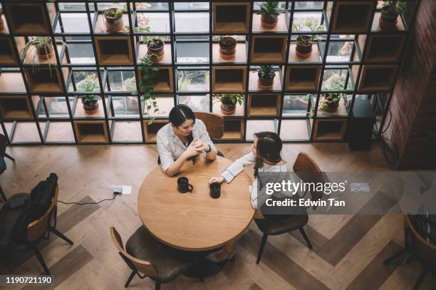 top angle of 2 office white collar female worker taking a coffee break at the office cafeteria having discussion - asian discuss stock pictures, royalty-free photos & images