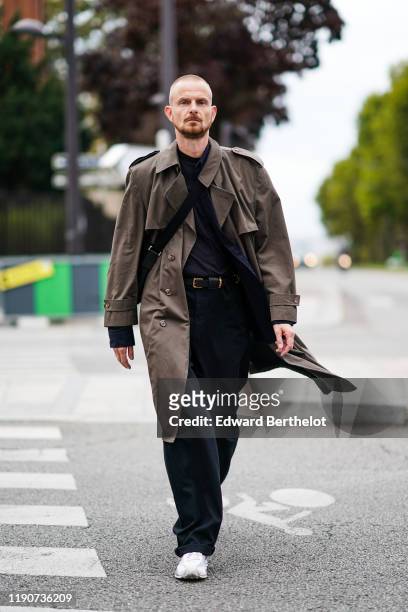 Guest wears a khaki trench coat, black pants, a belt, white sneakers, outside Ann Demeulemeester, during Paris Fashion Week - Womenswear Spring...