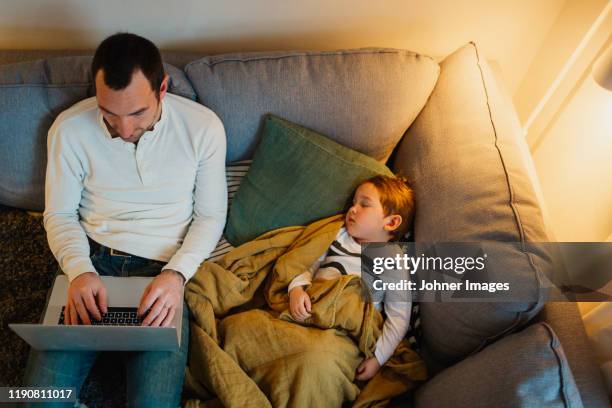 father using laptop in living room while daughter sleeping next to him - digital devices beside each other stockfoto's en -beelden