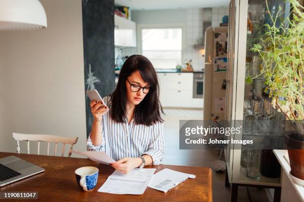woman with laptop and smartphone in dining room - woman using smartphone with laptop stock-fotos und bilder