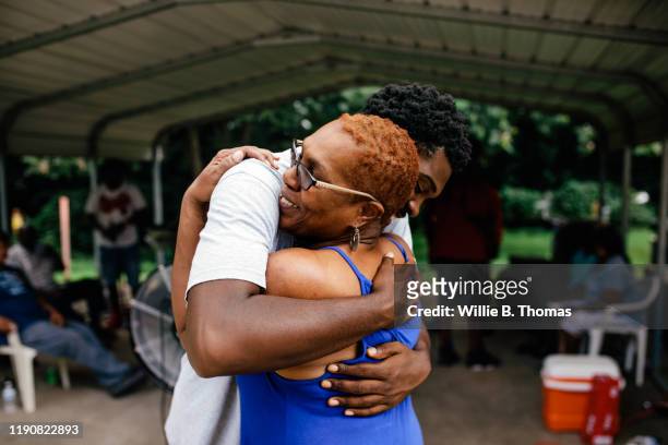 middle aged black mother hugging her son - zoon stockfoto's en -beelden