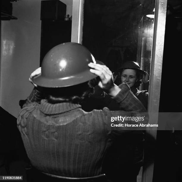 Nippy' or waitress at a J Lyons & Co tea shop in London getting dressed for her fire watch duty during World War II, March 1941. She will look out...