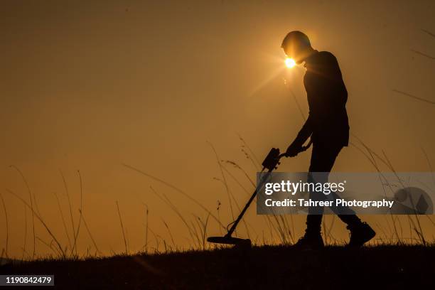 a young man using recreational metal detector to find treasure - treasure hunt photos et images de collection