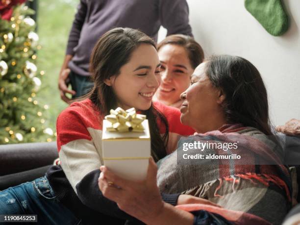 cute teenage girl giving christmas gift to grandmother - mexican christmas stock pictures, royalty-free photos & images