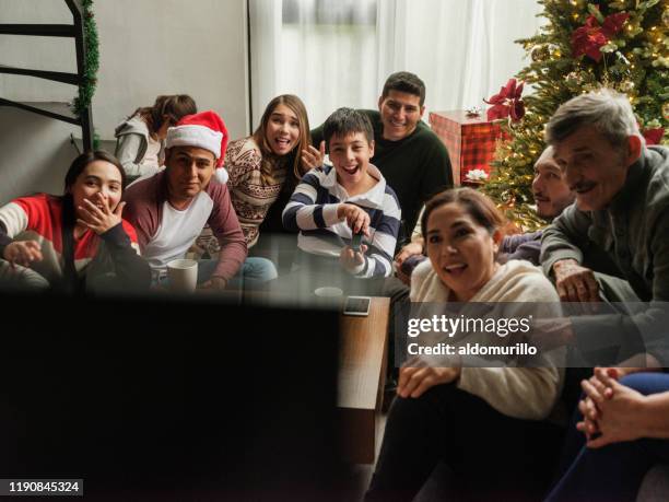 fun latin family watching television in living room - mexican christmas stock pictures, royalty-free photos & images