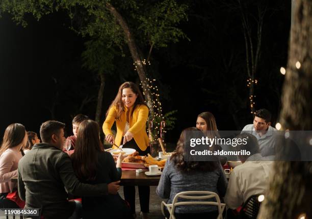 latin mother standing and serving food at table with family - mexican christmas stock pictures, royalty-free photos & images