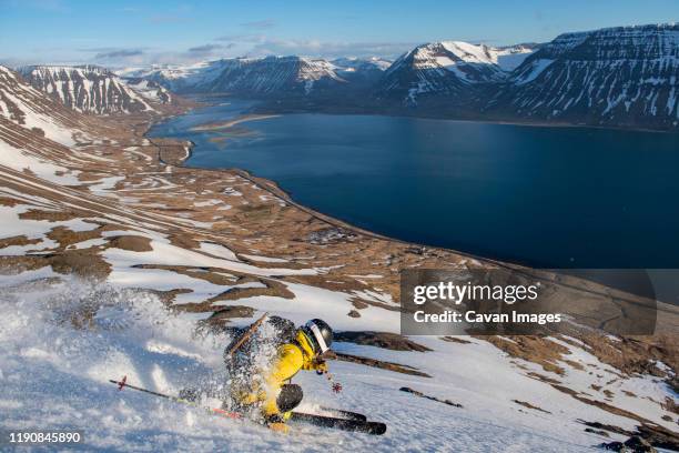 a man backcountry skiing to the ocean in iceland. - fiordi occidentali islanda foto e immagini stock