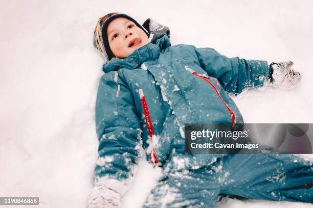 happy boy with arms outstretched lying in snow during winter - teal parka stock pictures, royalty-free photos & images