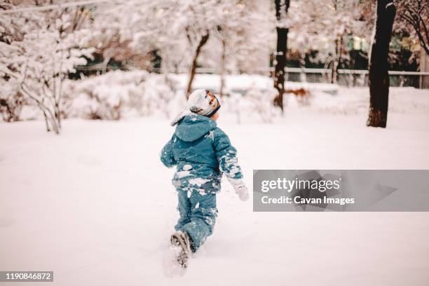 rear view of boy running in snow covered field in park in winter - teal parka stock pictures, royalty-free photos & images