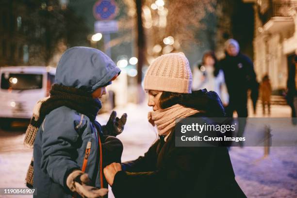 mother communicating with son while zipping his jacket in street - parka coat stock-fotos und bilder