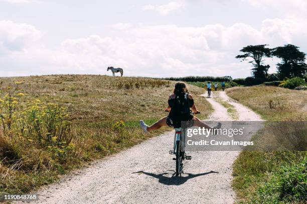 pretty young woman riding bicycle with open legs in a country road - bretagne photos et images de collection