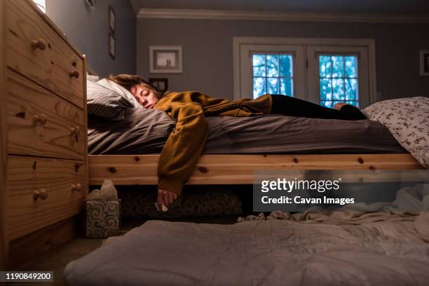 disheveled young woman laying in bed holding tissue and tissue box - illness stock pictures, royalty-free photos & images