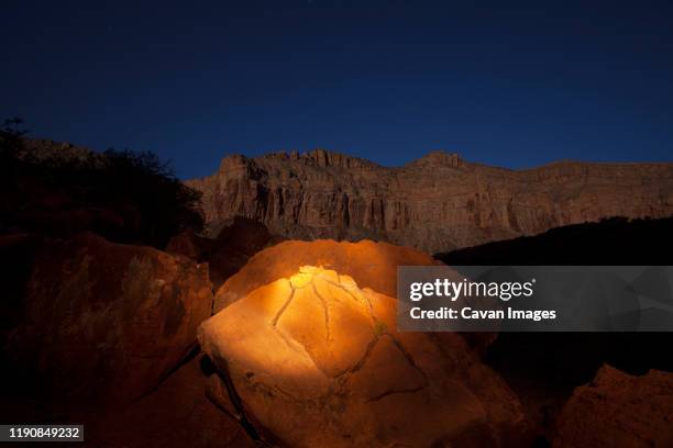 the orange glow of a flashlight illuminates a cracked rock at night - yellow light stock pictures, royalty-free photos & images