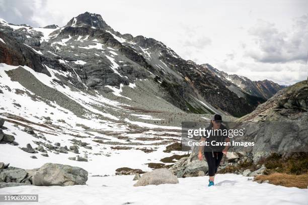 a women hikes up a snow field on a summer day in the mountains for british columbia. - hurley stick stock pictures, royalty-free photos & images