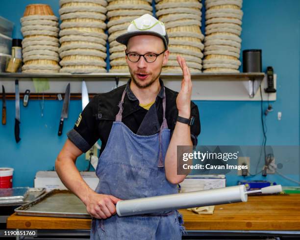a professional baker talks with rolling pin in hand in kitchen - rolling pin stock pictures, royalty-free photos & images