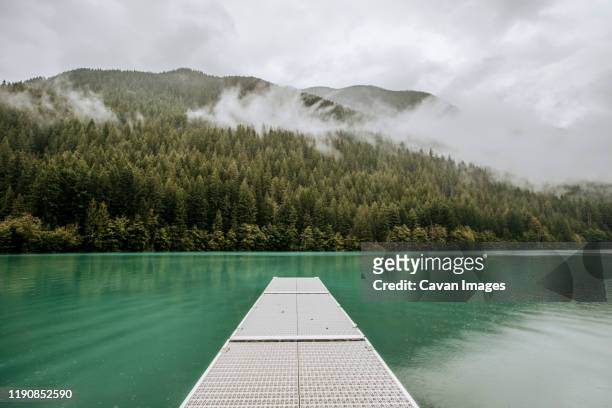 a dock on a glacial lake surrounded by misty mountains and forest - diablo lake stock-fotos und bilder