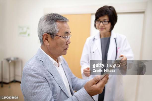 senior man reading electronic medical record being held by female doctor in hospital - medical examination room stock pictures, royalty-free photos & images