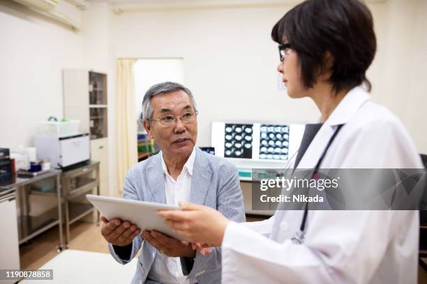 female doctor showing electronic medical record to senior male patient in hospital - medical examination room stock pictures, royalty-free photos & images