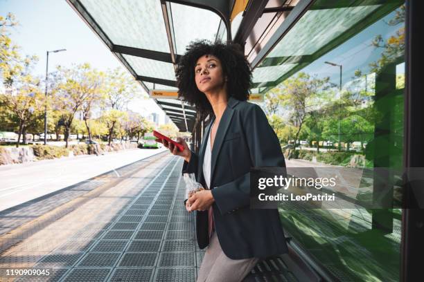 business afro amerikanische frau an bushaltestelle in der innenstadt - bushaltestelle stock-fotos und bilder