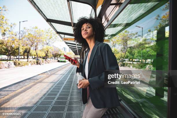 mujer afroamericana de negocios en parada de autobús en el centro de la ciudad - parada de autobús fotografías e imágenes de stock